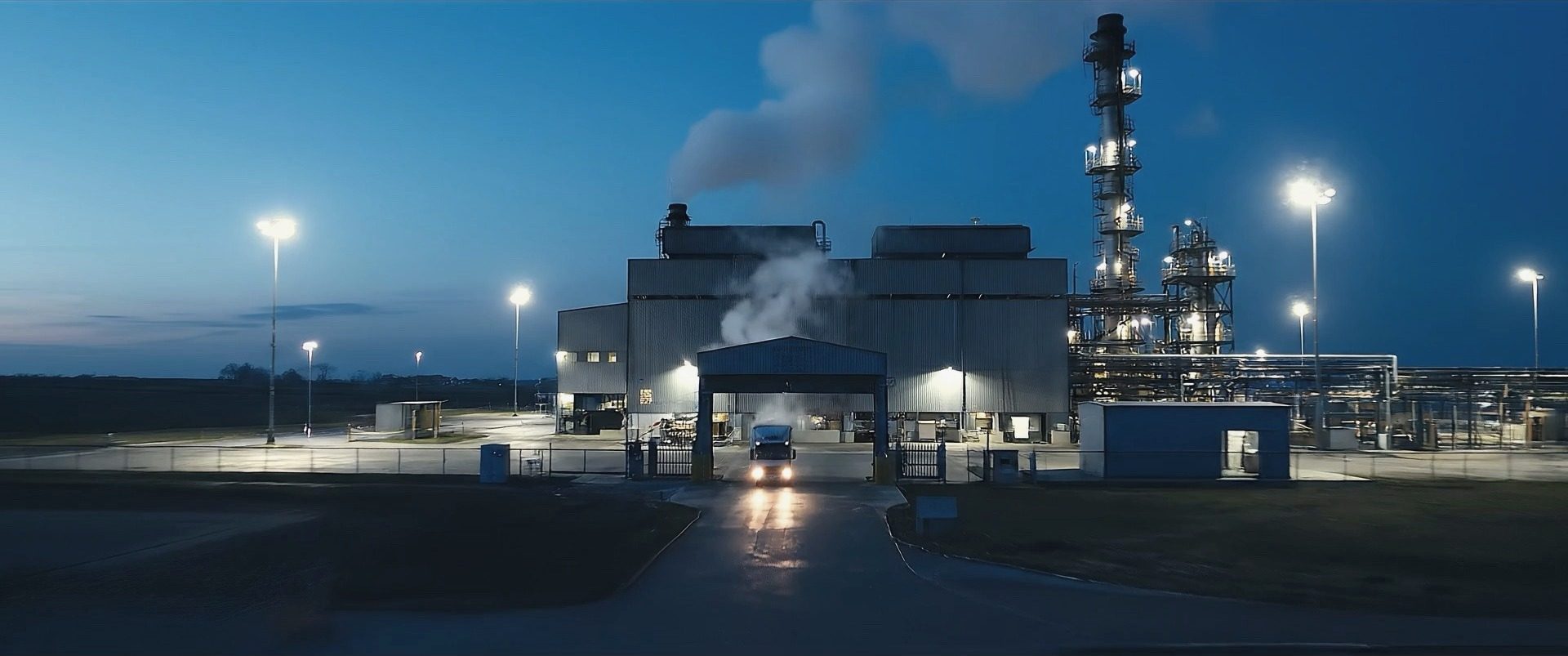 Process plant at dusk with a truck leaving through the lit gate
